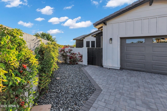 view of property exterior featuring board and batten siding, an attached garage, fence, and a gate