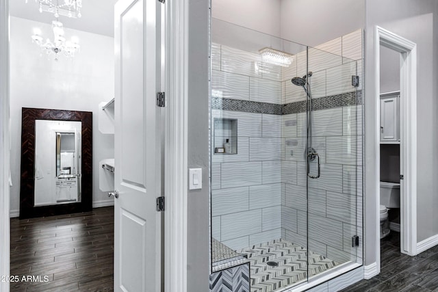 full bath with a shower stall, toilet, wood finished floors, and a notable chandelier