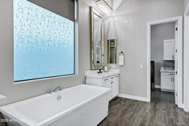 bathroom featuring baseboards, wood finished floors, a freestanding tub, and vanity