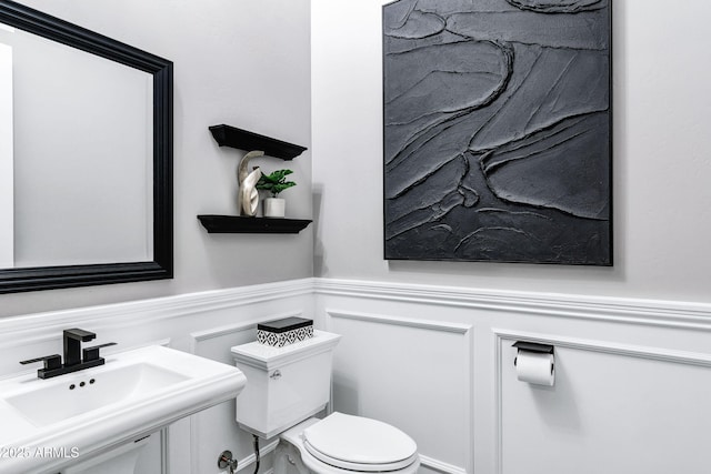 half bath featuring a decorative wall, toilet, a sink, and a wainscoted wall