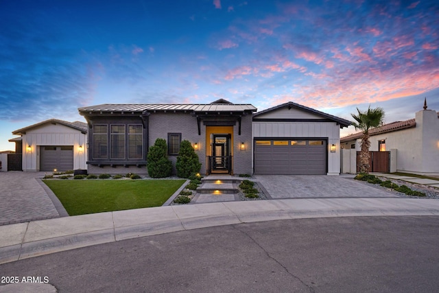 view of front of home with a standing seam roof, decorative driveway, fence, a front lawn, and an attached garage
