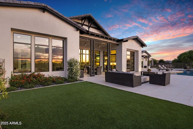 back of house at dusk with stucco siding, an outdoor hangout area, a ceiling fan, a patio area, and a yard