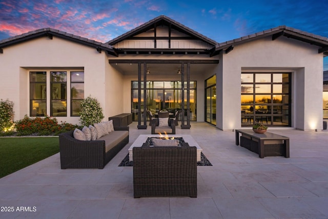back of house at dusk with a patio, an outdoor living space with a fire pit, and stucco siding