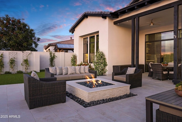 patio terrace at dusk featuring fence, an outdoor living space with a fire pit, and a ceiling fan
