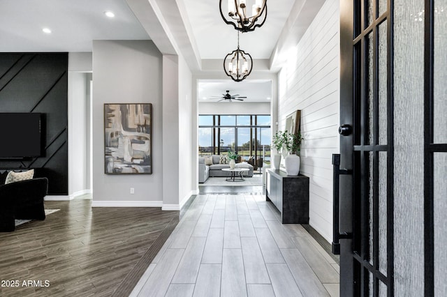 entryway with wood finished floors, baseboards, recessed lighting, a tray ceiling, and ceiling fan with notable chandelier