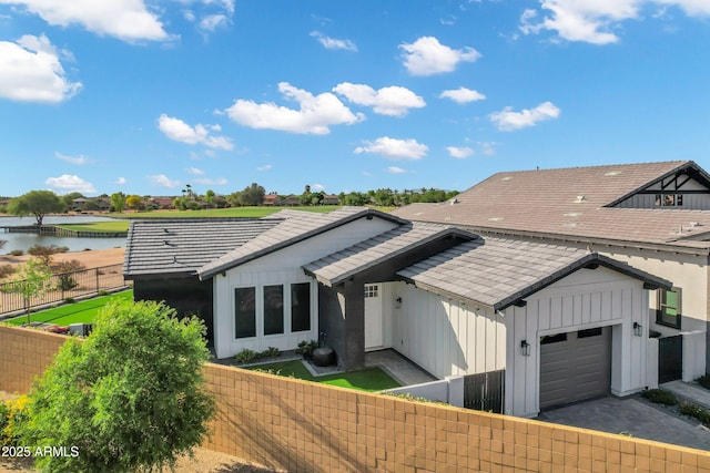 view of front of house featuring board and batten siding, a water view, an attached garage, and fence private yard