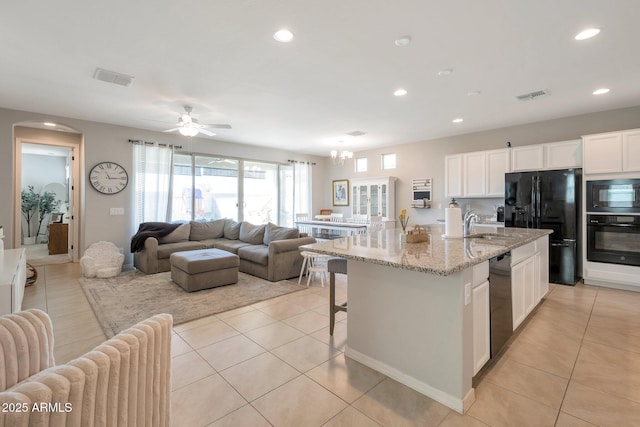 kitchen featuring light stone countertops, black appliances, light tile patterned floors, white cabinets, and an island with sink