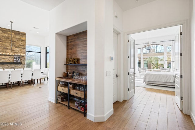 hallway featuring baseboards, a high ceiling, wood finished floors, and a notable chandelier