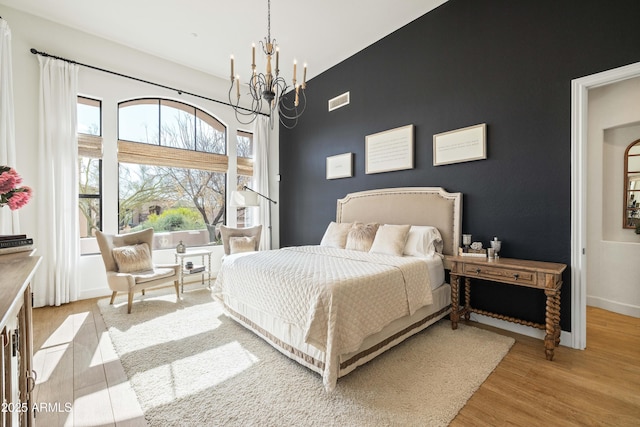 bedroom featuring a notable chandelier, light wood finished floors, visible vents, an accent wall, and baseboards