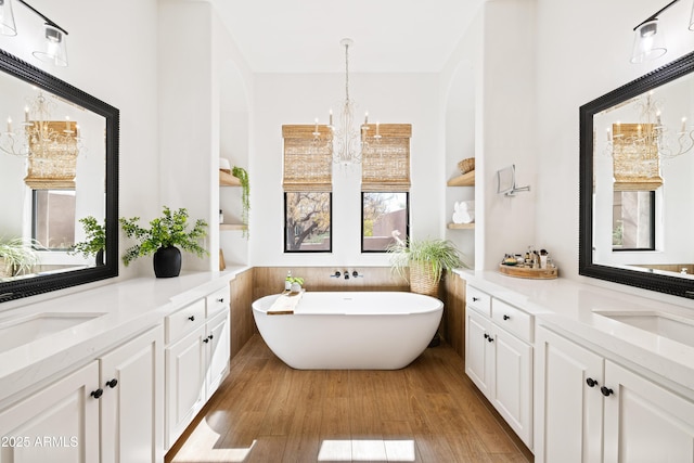 full bathroom featuring a chandelier, a freestanding tub, a sink, two vanities, and wood finished floors