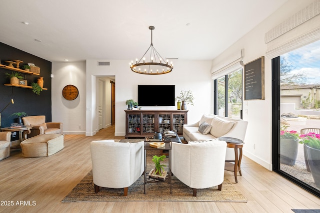 living area featuring light wood-type flooring, an inviting chandelier, baseboards, and visible vents