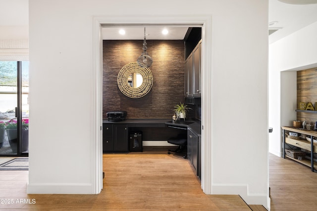 interior space featuring light wood finished floors, built in desk, and baseboards