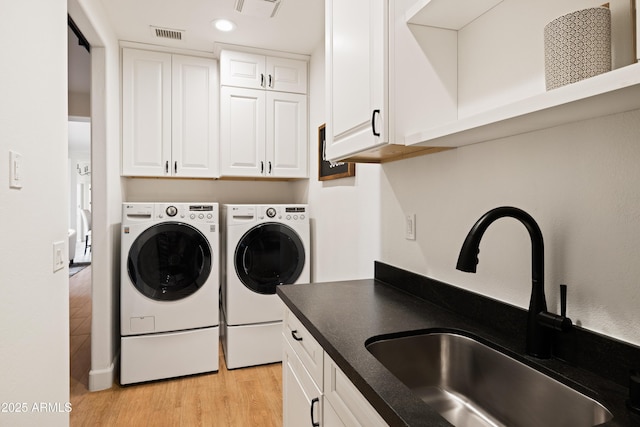 clothes washing area featuring visible vents, cabinet space, light wood-style flooring, a sink, and washer and dryer