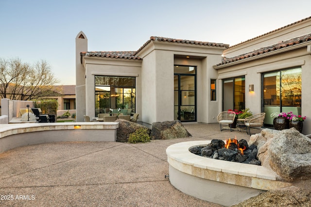 back of property with stucco siding, a tiled roof, a fire pit, and a patio