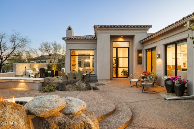 rear view of house featuring a tile roof, exterior kitchen, stucco siding, a chimney, and a patio area