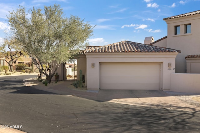 mediterranean / spanish-style house featuring a garage, concrete driveway, a tile roof, a gate, and stucco siding