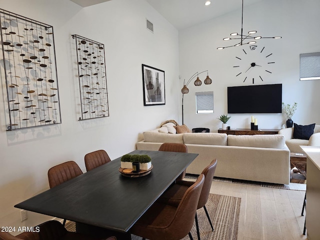 dining space with high vaulted ceiling, an inviting chandelier, and light hardwood / wood-style floors