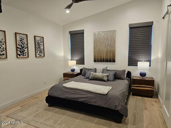 bedroom with baseboards, a barn door, lofted ceiling, recessed lighting, and wood finished floors