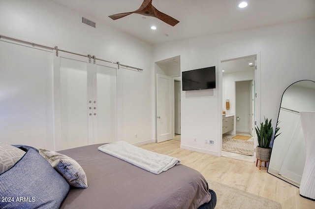 bedroom with a barn door, ceiling fan, light hardwood / wood-style flooring, and ensuite bath