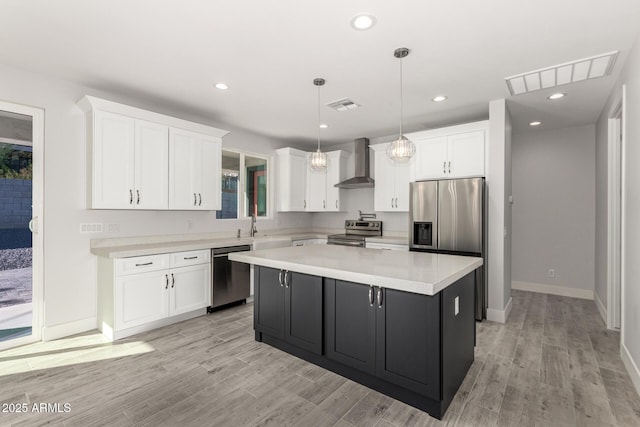 kitchen featuring a center island, decorative light fixtures, stainless steel appliances, wall chimney range hood, and white cabinets