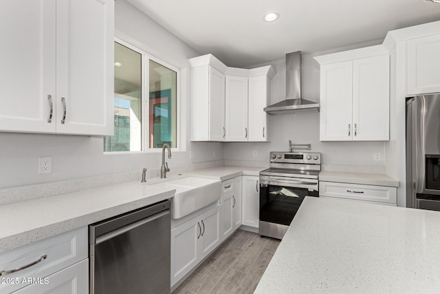 kitchen featuring light stone countertops, wall chimney range hood, white cabinetry, appliances with stainless steel finishes, and sink