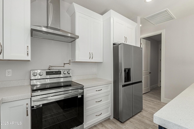 kitchen with appliances with stainless steel finishes, light hardwood / wood-style flooring, white cabinetry, and wall chimney exhaust hood