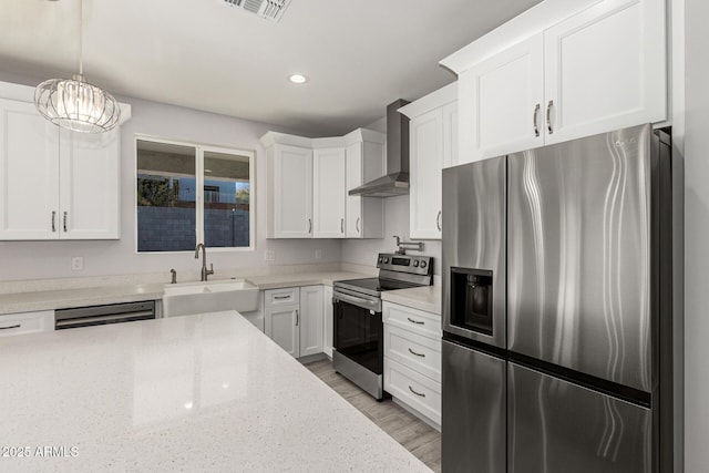 kitchen with wall chimney exhaust hood, decorative light fixtures, white cabinetry, appliances with stainless steel finishes, and sink