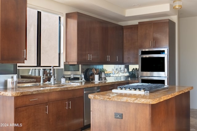 kitchen with light stone counters, appliances with stainless steel finishes, sink, and a center island