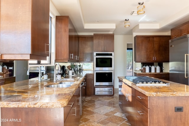 kitchen with light stone countertops, stainless steel appliances, a raised ceiling, and a kitchen island