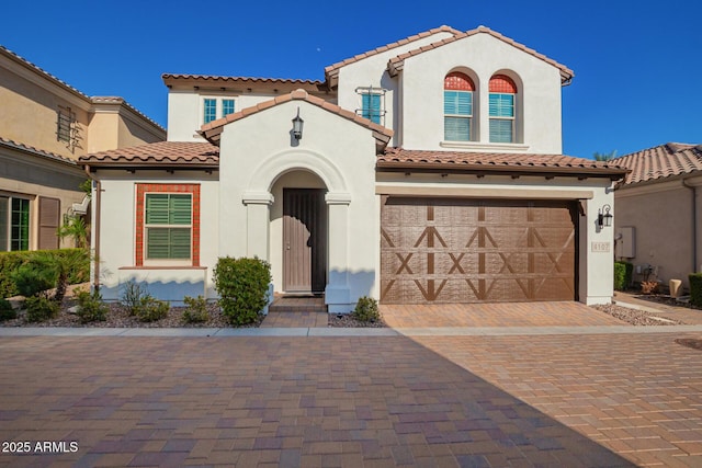 mediterranean / spanish house with stucco siding, an attached garage, and decorative driveway