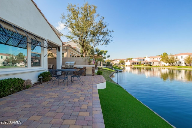 view of patio with a water view, area for grilling, fence, a residential view, and exterior kitchen