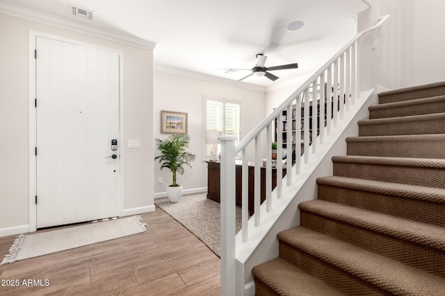 foyer featuring light wood finished floors, visible vents, crown molding, ceiling fan, and stairway