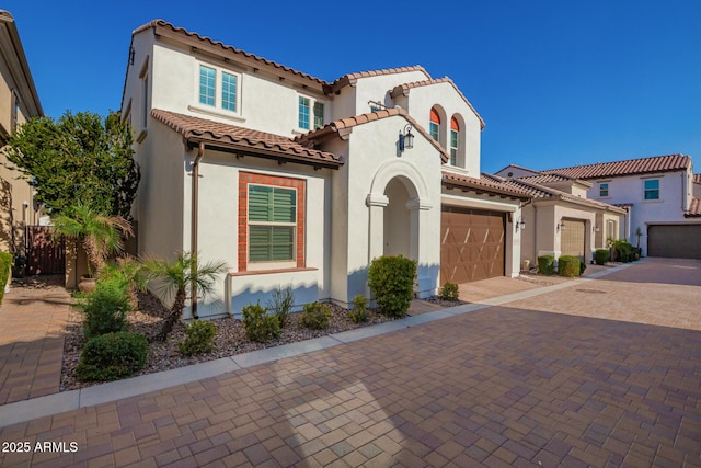 mediterranean / spanish-style home with a tile roof, decorative driveway, an attached garage, and stucco siding