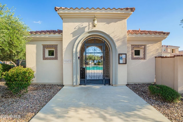 view of exterior entry featuring a gate, stucco siding, a tiled roof, and fence