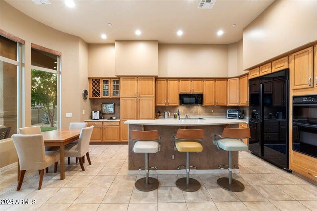 kitchen with light tile patterned floors, a center island with sink, black appliances, a kitchen breakfast bar, and a high ceiling