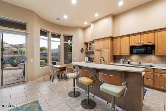 kitchen with a kitchen island with sink, a breakfast bar area, a towering ceiling, black appliances, and light tile patterned floors