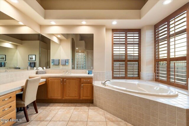 bathroom featuring tiled tub, vanity, a tray ceiling, and tile patterned floors