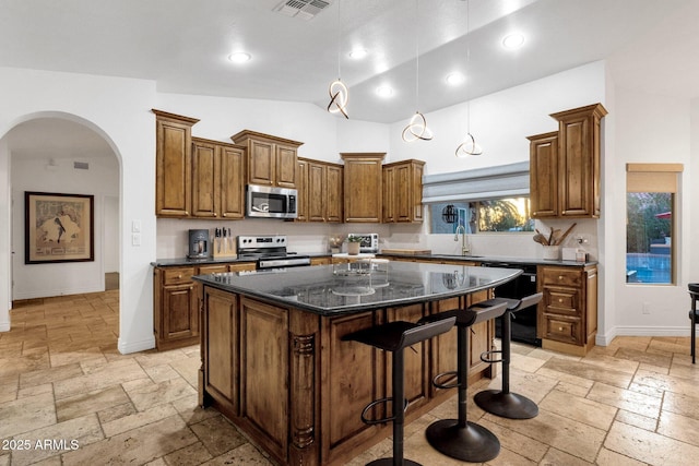 kitchen featuring visible vents, stone tile flooring, appliances with stainless steel finishes, arched walkways, and a sink