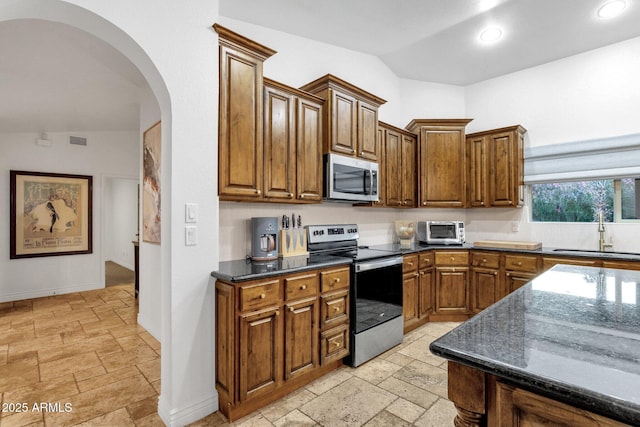kitchen featuring a sink, arched walkways, visible vents, stone tile flooring, and appliances with stainless steel finishes