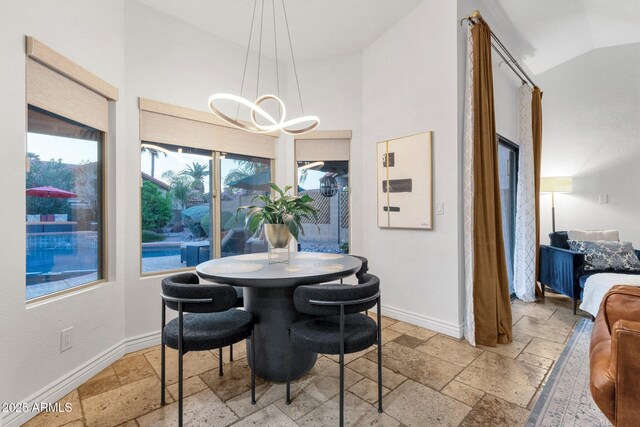 dining space featuring high vaulted ceiling, stone tile floors, baseboards, and a chandelier