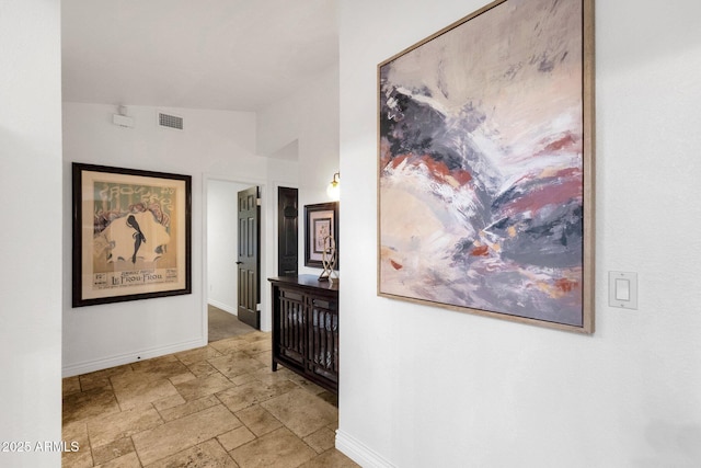 hall featuring baseboards, visible vents, vaulted ceiling, and stone tile floors