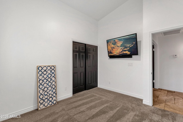 carpeted spare room with baseboards, visible vents, and high vaulted ceiling
