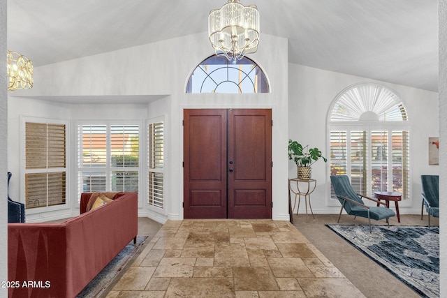 entrance foyer featuring an inviting chandelier, stone tile flooring, and lofted ceiling