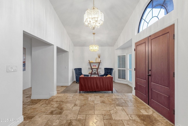 entryway featuring baseboards, high vaulted ceiling, stone tile floors, and an inviting chandelier
