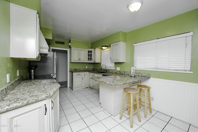 kitchen with white cabinets, a breakfast bar, light stone counters, and sink