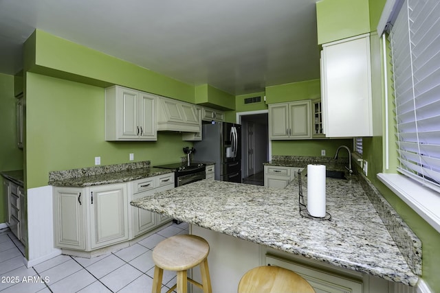 kitchen featuring a breakfast bar, black range with electric stovetop, sink, stainless steel fridge, and kitchen peninsula