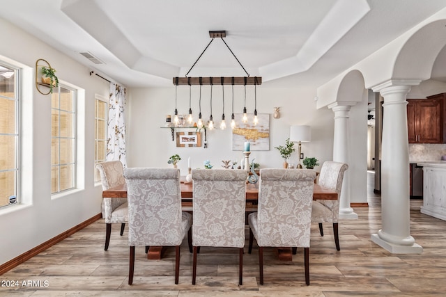 dining space with plenty of natural light, light hardwood / wood-style flooring, ornate columns, and a raised ceiling