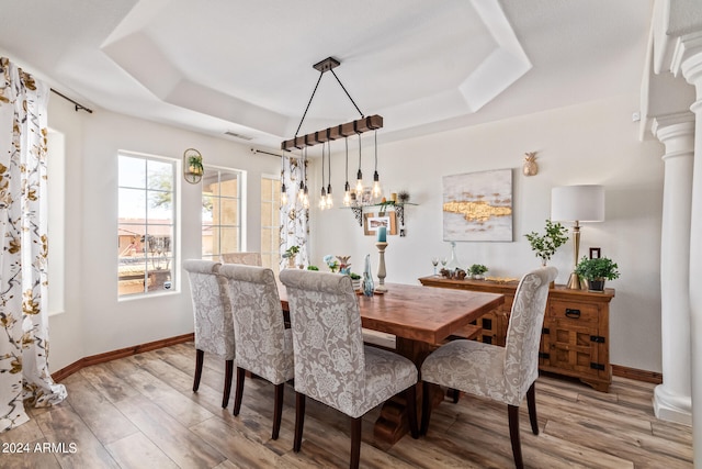 dining room featuring a raised ceiling, light hardwood / wood-style floors, and ornate columns