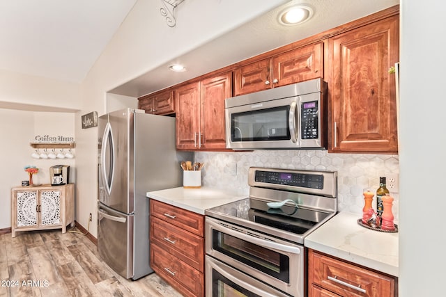 kitchen with lofted ceiling, backsplash, light hardwood / wood-style floors, and appliances with stainless steel finishes