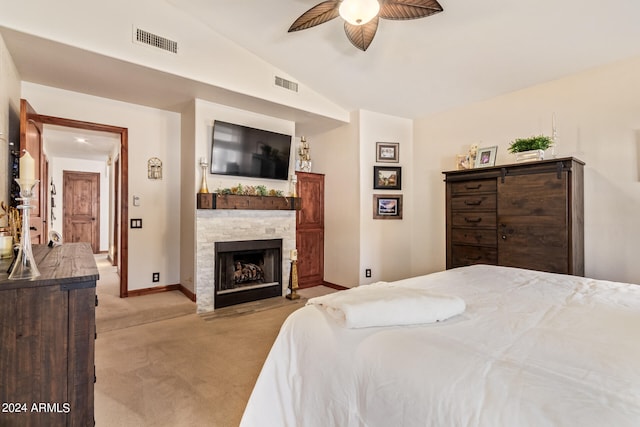 bedroom featuring light carpet, lofted ceiling, a stone fireplace, and ceiling fan